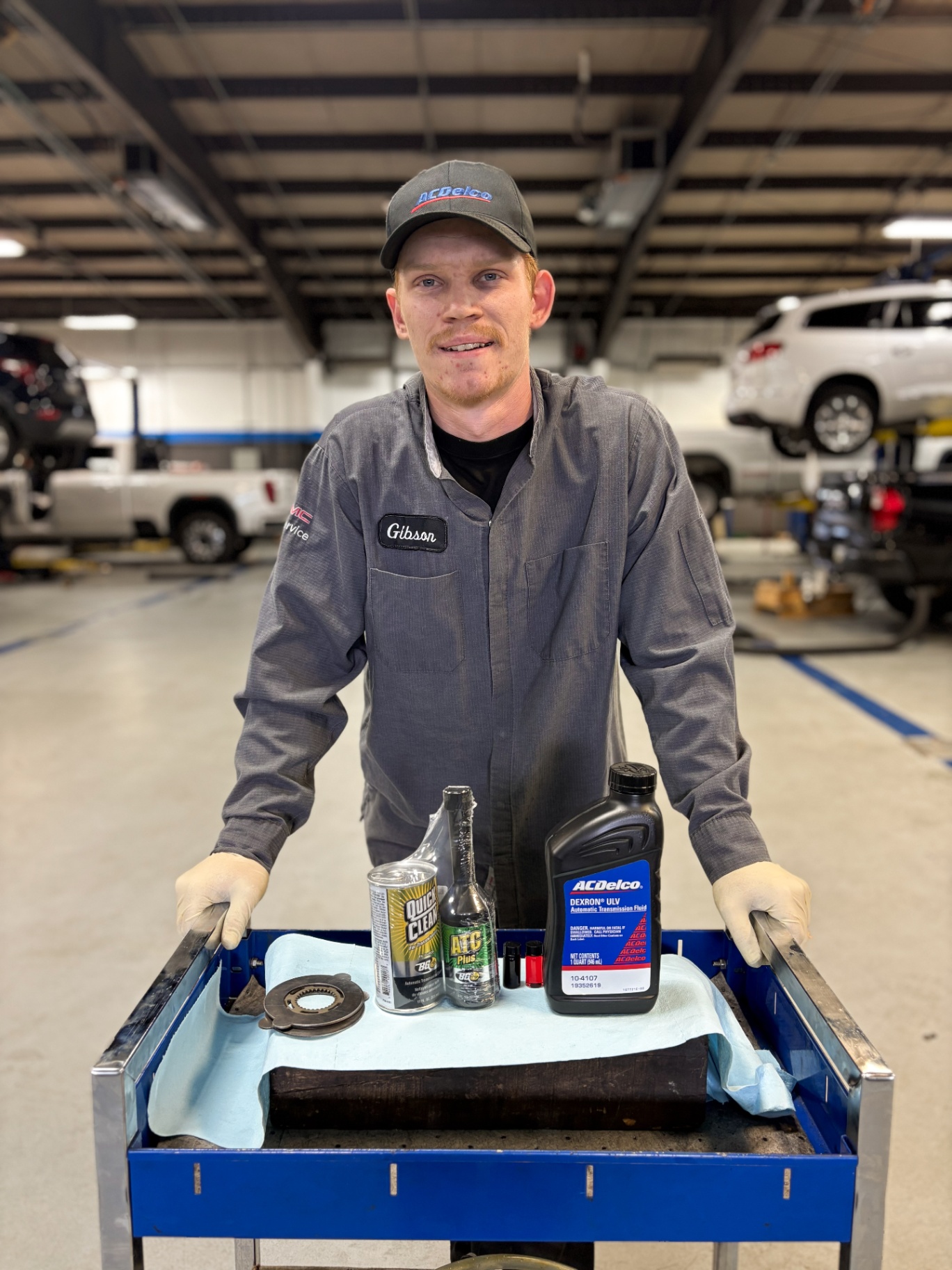 Technician with a service tray of parts inside a dealership shop.