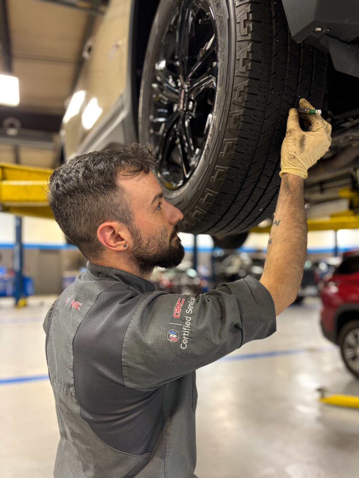 Patriot GMC Certified Service tech measuring tire tread depth on a lifted GMC