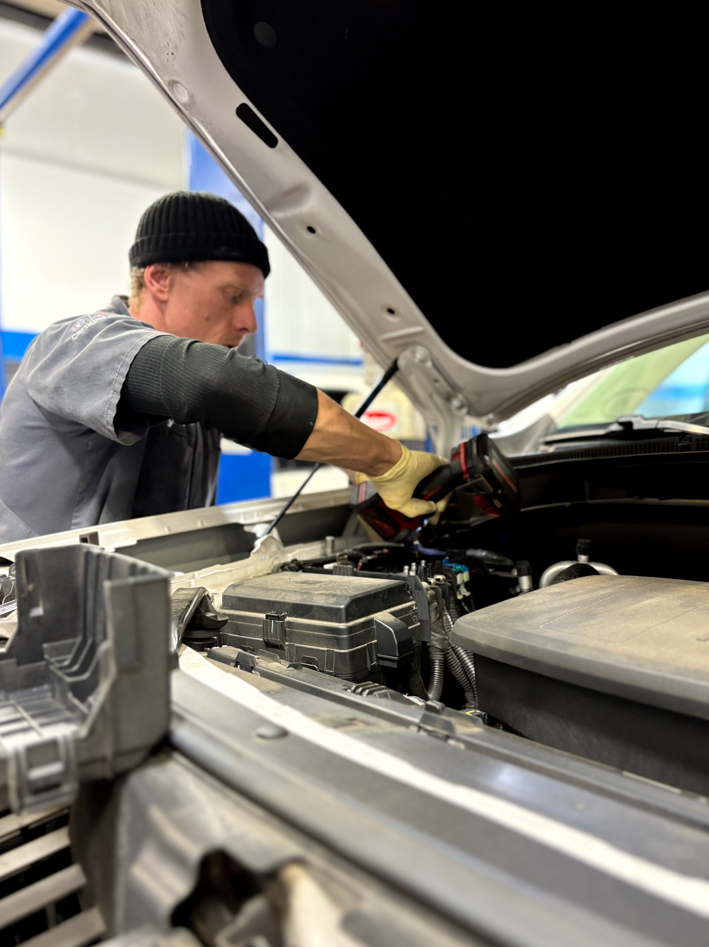 Technician performing diagnostic work under the hood of a vehicle.