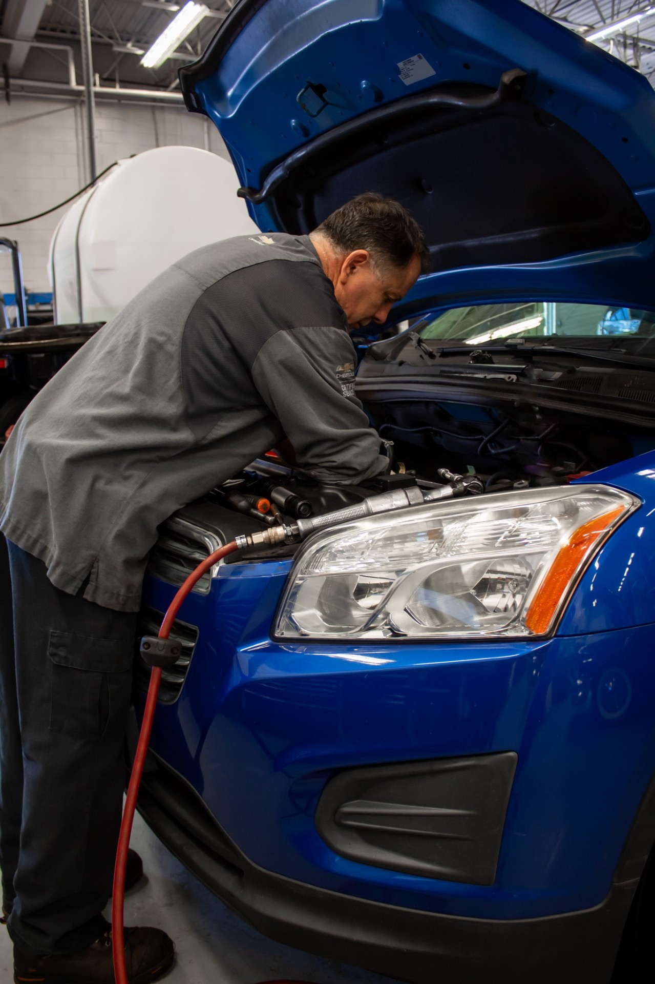 Technician diagnosing a Chevrolet vehicle in a dealership service bay.