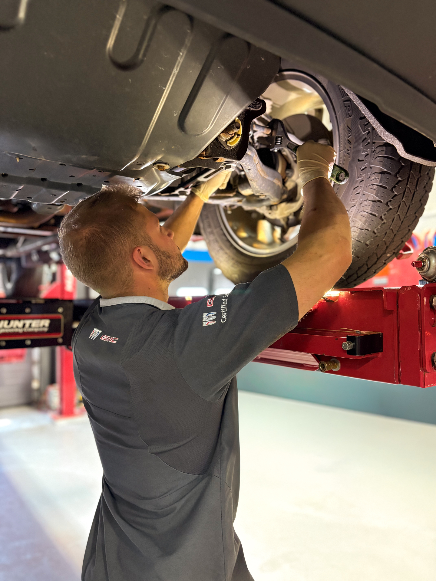 Patriot Buick GMC Certified Service technician wrenching on the underbody at a Hunter alignment rack
