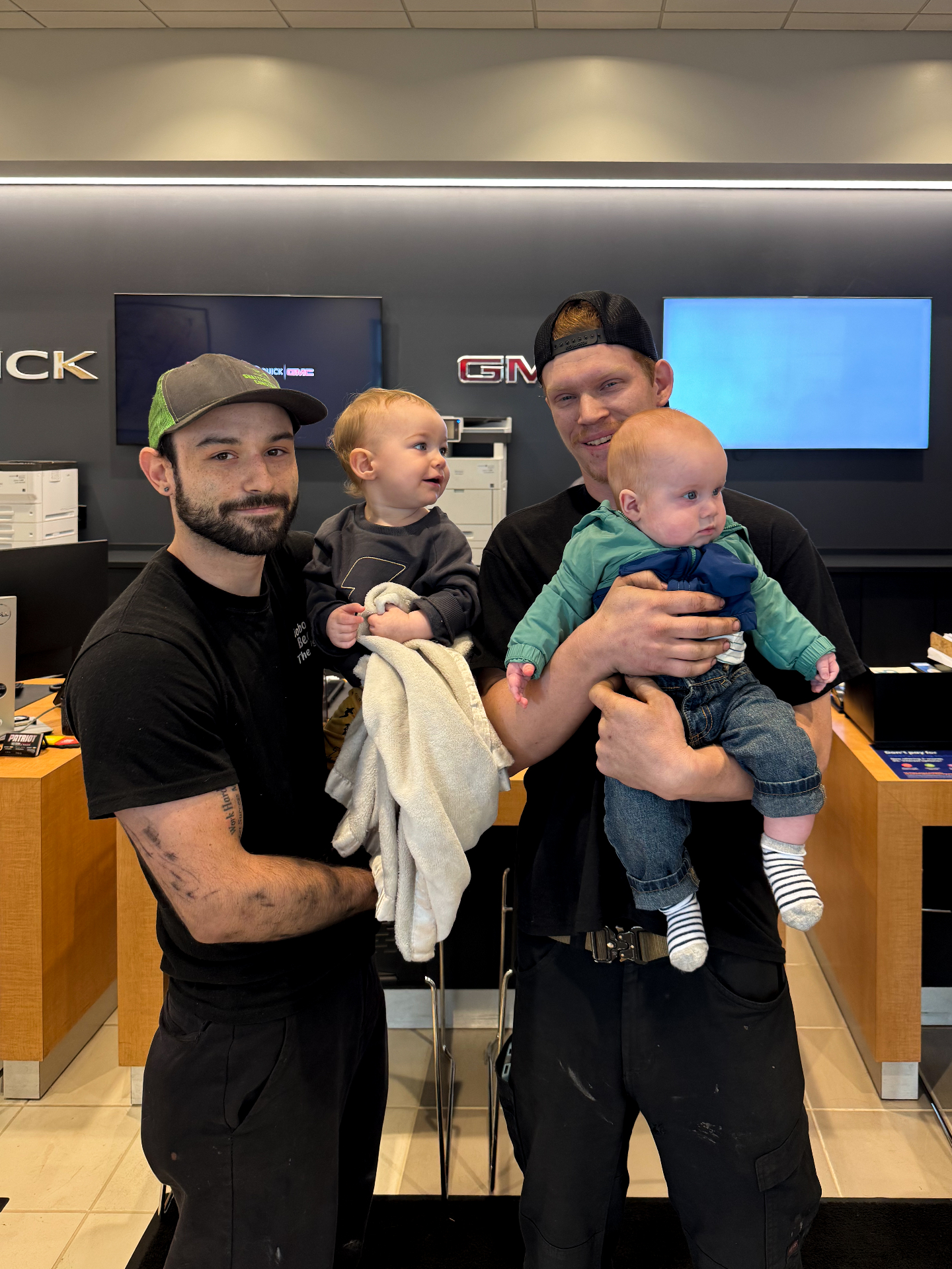 Two Patriot technicians holding their young children in the dealership showroom